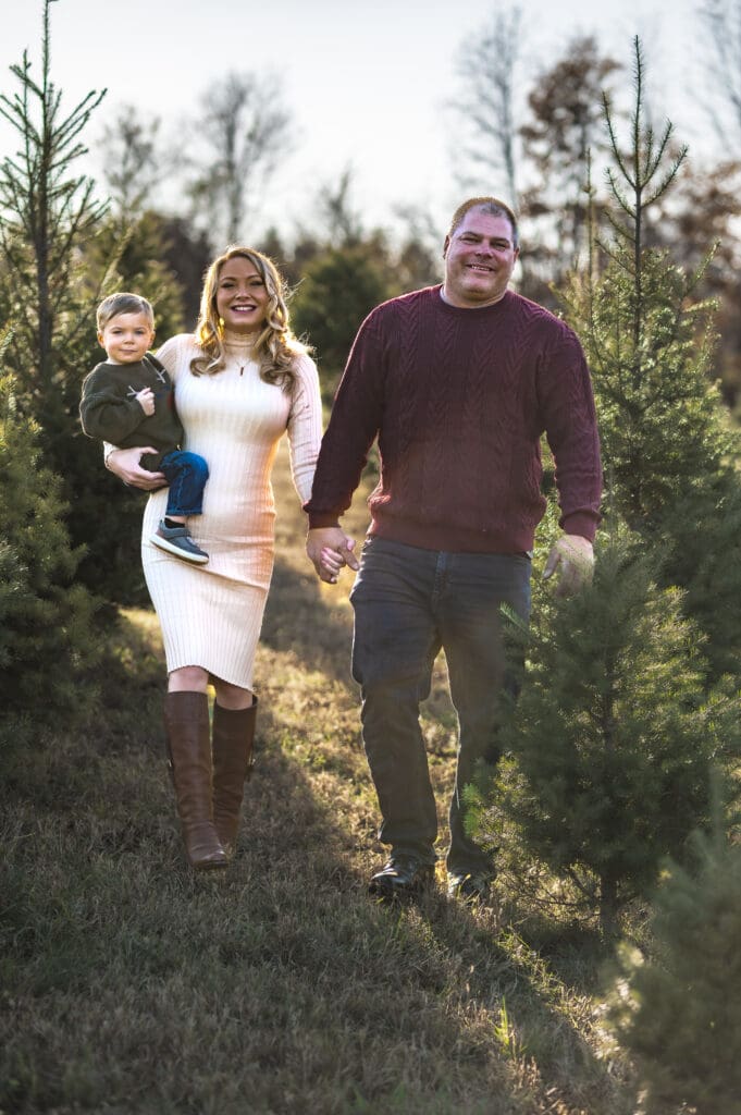 A family of three walks toward the camera, the parents are holding hands and the mom has her son on her hip, everyone is smiling. 