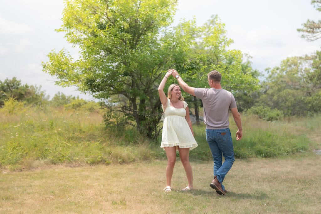 A photo of a young couple dancing in a grassy field on a sunny day.