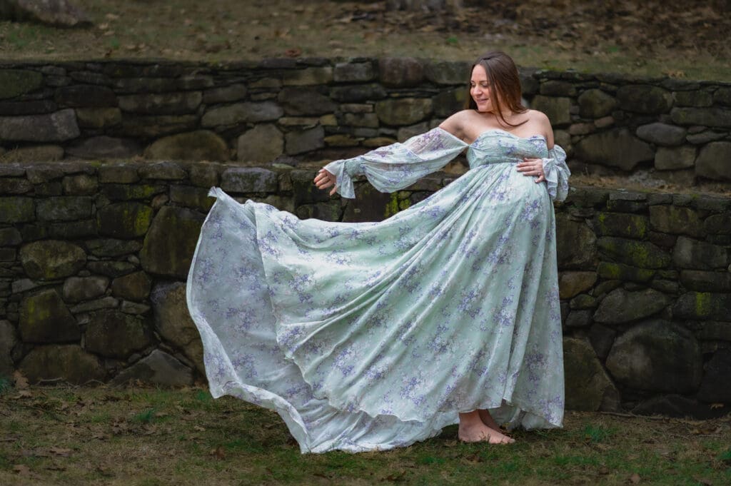 A pregnant woman in a flowing dress is looking at her train blowing in the wind outside.